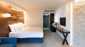 A modern hotel room with a large bed, a seating area, a small table with a vase of flowers, and a mounted TV. - Shefayim Hotel (Hod HaSharon)