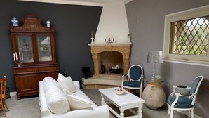 Una sala de estar con un sofá blanco, una mesa de centro blanca, un sillón azul, un sillón blanco, una chimenea y un aparador de madera.