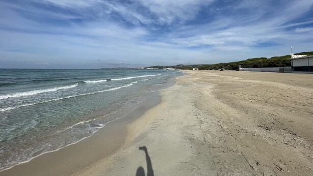 Una playa con cielos despejados, olas suaves y una vista distante de colinas.