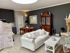 Ein Wohnzimmer mit einem weißen Sofa, einem Esstisch mit Stühlen, einem Holzschrank und einer dekorativen Glasvitrine.