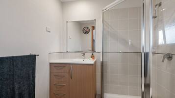 Een badkamer met een douche, wastafel en spiegel.
