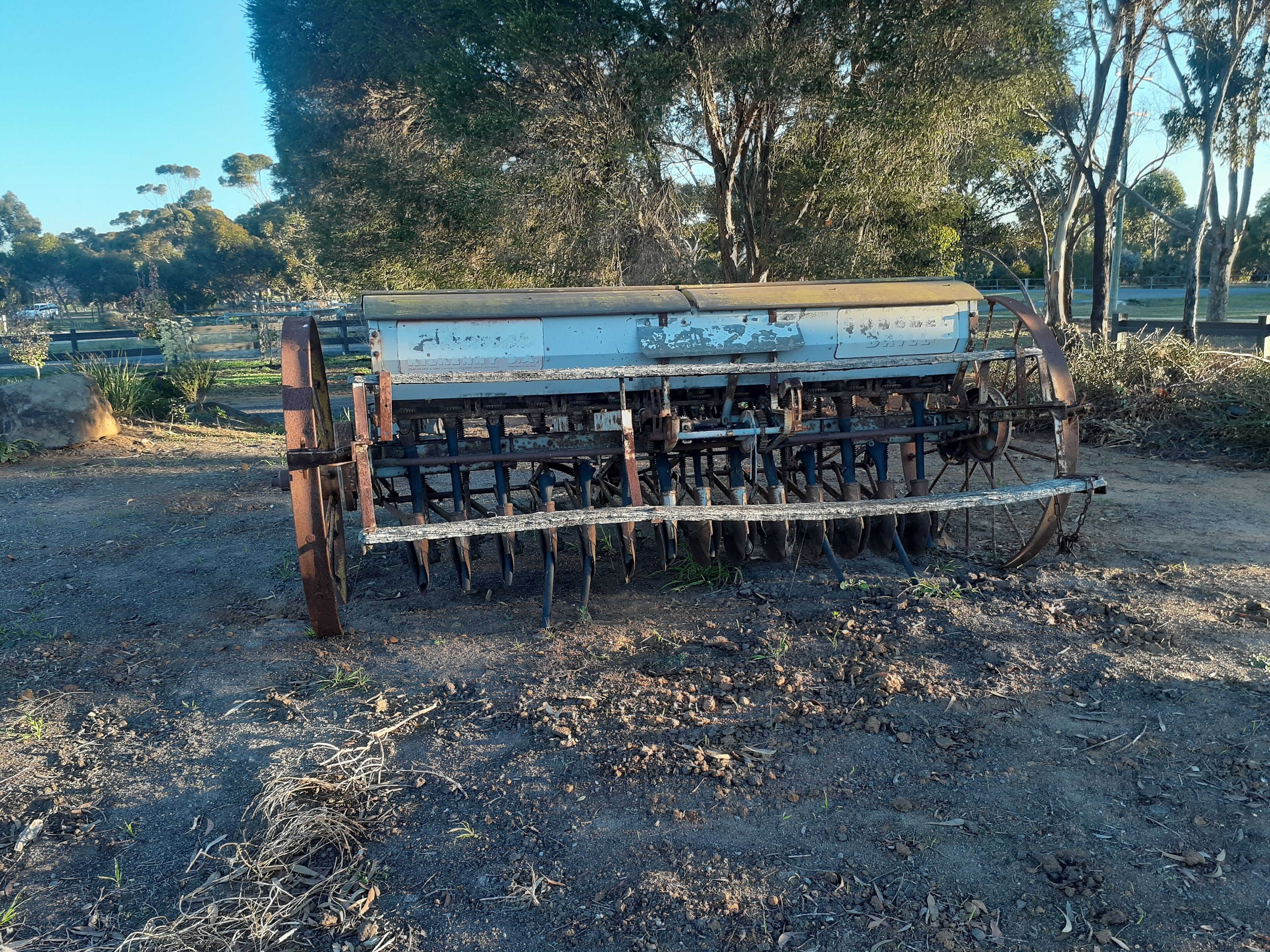 An old, rusted plow in a field with trees in the background.