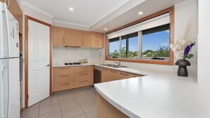 Una cocina moderna con armarios de madera, encimera blanca y ventana con vistas a zonas verdes.