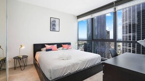 A modern hotel room with a large bed, a desk, and a view of tall buildings.