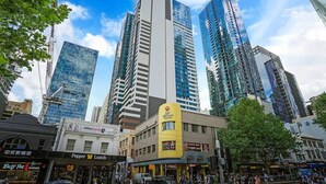 A city street with tall buildings, a pedestrian crossing, and various storefronts including a restaurant and a bank.