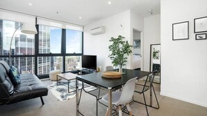 A modern living room with a sofa, a dining table with chairs, a TV, and a large window with a city view.