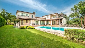A large, two-story stone house with a swimming pool, surrounded by a well-maintained lawn and trees. - Luxury 4-BR Villa with Pool, Ensuite Sauna, and Stunning Sea & Forest Views (Višnjan)