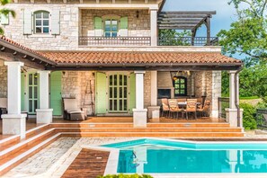 A two-story stone building with a covered patio, outdoor seating, and a swimming pool.