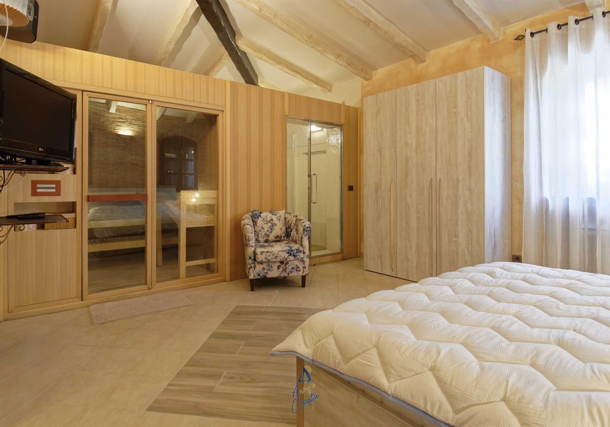 A bedroom with a bed, a television, a chair, and a sliding glass door leading to a bathroom.