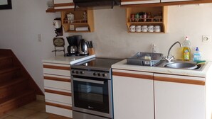 A kitchen with a stove, oven, sink, and wooden cabinets. - La Chaumière, Séjour Paisible (Sourdeval)
