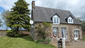 A stone house with a sloped roof, wooden shutters, and a satellite dish. - La Chaumière, Séjour Paisible (Sourdeval)