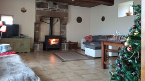 A cozy living room with a stone fireplace, a television, a sofa, and a Christmas tree. - La Chaumière, Séjour Paisible (Sourdeval)
