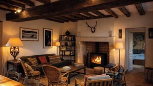 A cozy living room with a fireplace, wooden beams, a bookshelf, and comfortable seating.