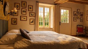 A bedroom with a large bed, multiple framed animal prints on the wall, and a window with curtains.