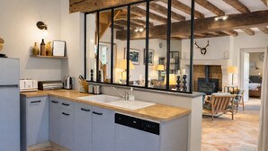A modern kitchen with a central island, built-in dishwasher, and a large window with wooden beams above.