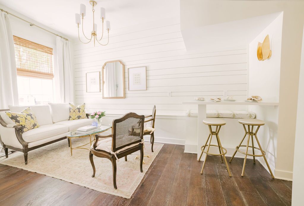 Un salon lumineux avec un canapé blanc, une table basse en bois et deux tabourets de bar.