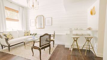 Un salon lumineux avec un canapé blanc, une table basse en bois et deux tabourets de bar.