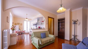 A spacious living area with a sofa, a dining table with chairs, and a kitchen in the background.