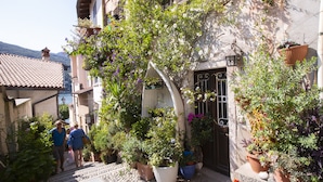 A narrow alley with steps leading to a building entrance, surrounded by potted plants and flowers. - Muffy (Stresa)
