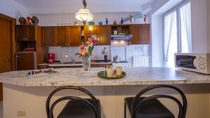 A kitchen with wooden cabinets, a marble countertop, a microwave, and a coffee maker. - Muffy (Stresa)