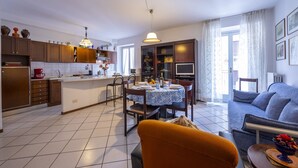 A modern kitchen with a dining area, a sofa, and a TV. - Muffy (Stresa)