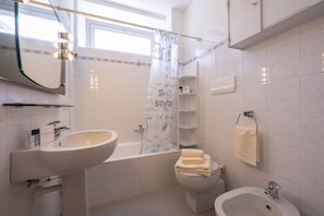 A bathroom with a bathtub, a toilet, and a bidet. There is a mirror above the sink, and a towel is hanging on the wall. - Muffy (Stresa)