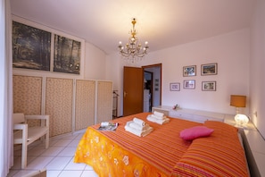A hotel room with a bed, a chandelier, a chair, a wardrobe, and a nightstand with a lamp. - Muffy (Stresa)