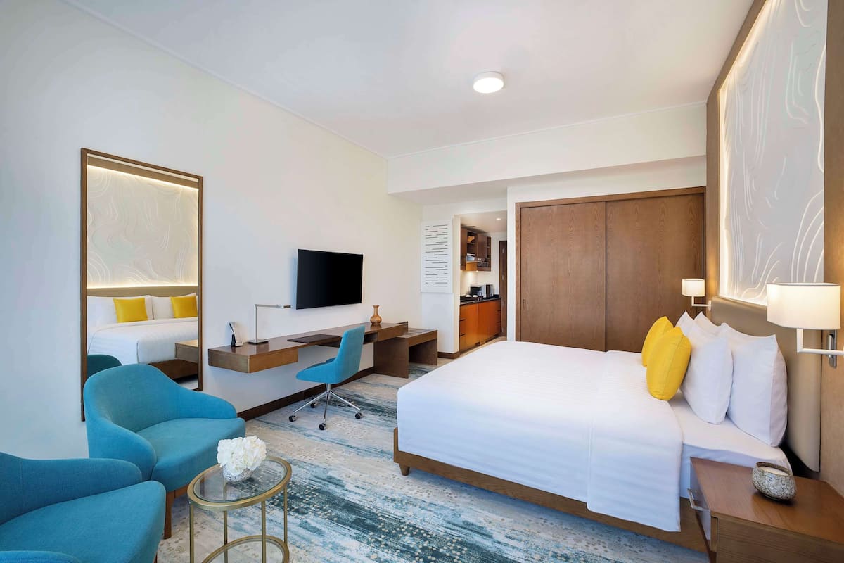 A hotel room with a large bed, a desk, a chair, a TV, and a wardrobe.