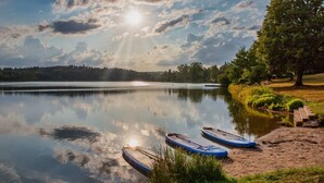 Ein ruhiger See mit zwei Stand-Up-Paddles am Ufer, umgeben von Bäumen und blauem Himmel.