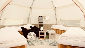 Ein Zelt mit zwei Betten, einem Ventilator und einem kleinen Tisch mit einer Lampe.