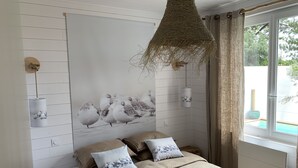 A bedroom with a bed, pillows, a wall-mounted light fixture, and a window with curtains. - Maison Avec Piscine (Saint-Jean-de-Monts)