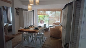 A dining area with a wooden table, white chairs, and a wicker sofa. - Maison Avec Piscine (Saint-Jean-de-Monts)