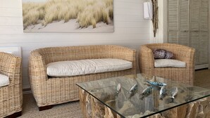 A room with wicker furniture, a glass coffee table with fish sculptures, and a beach-themed painting on the wall. - Maison Avec Piscine (Saint-Jean-de-Monts)