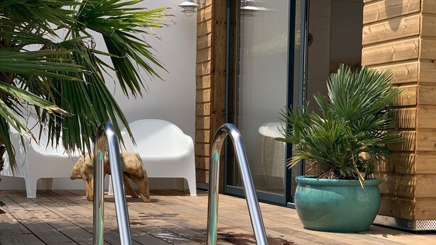 A swimming pool with metal handrails, a wooden deck, and potted plants. - Maison Avec Piscine (Saint-Jean-de-Monts)