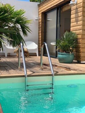 Ein Schwimmbecken mit Metallgeländern, einer Holzterrasse und Topfpflanzen.