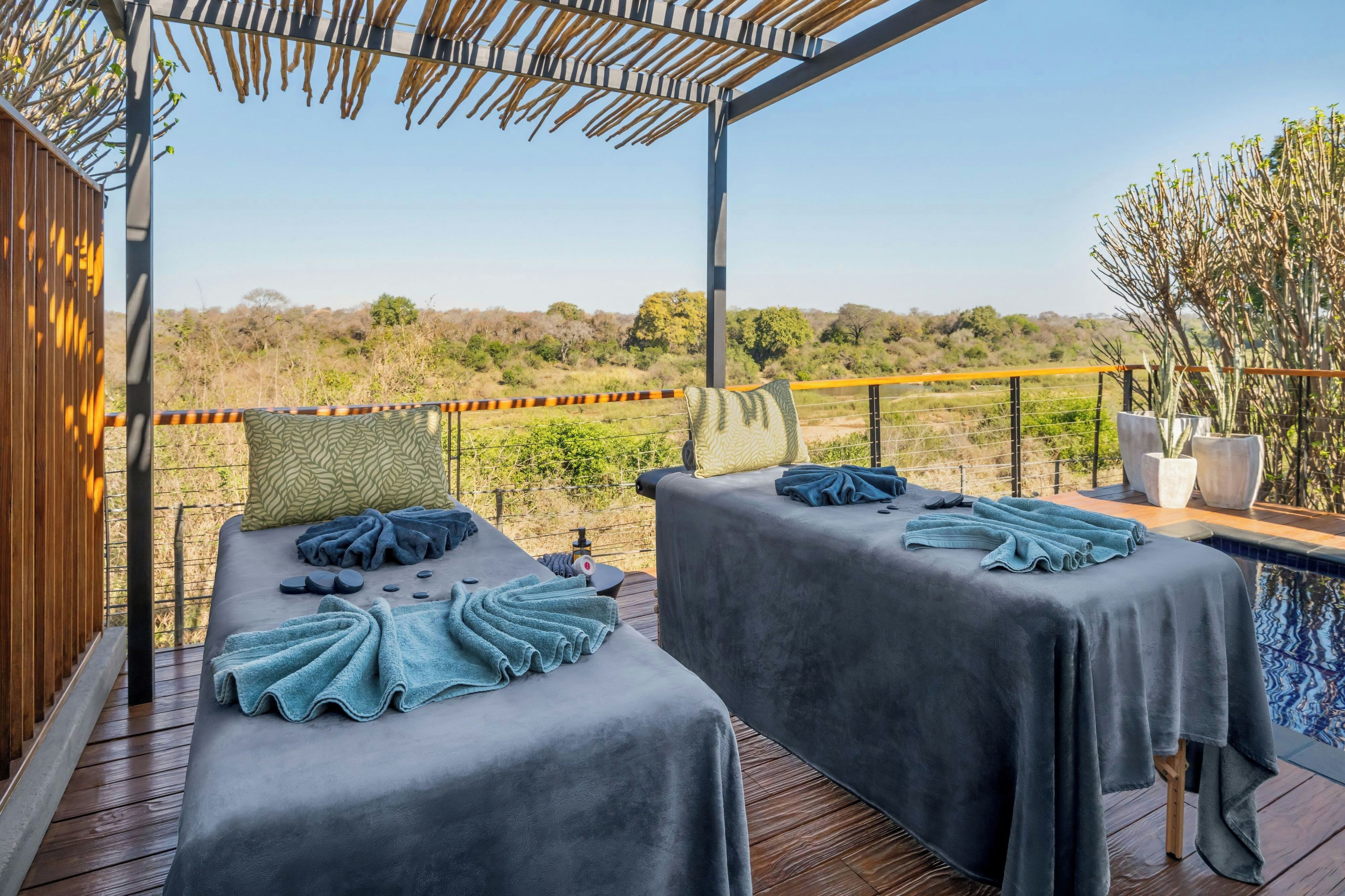 Ein Wellnessbereich mit zwei Massagetischen, einer Holzterrasse und Blick auf die umliegende Landschaft.