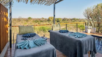 Ein Wellnessbereich mit zwei Massagetischen, einer Holzterrasse und Blick auf die umliegende Landschaft.