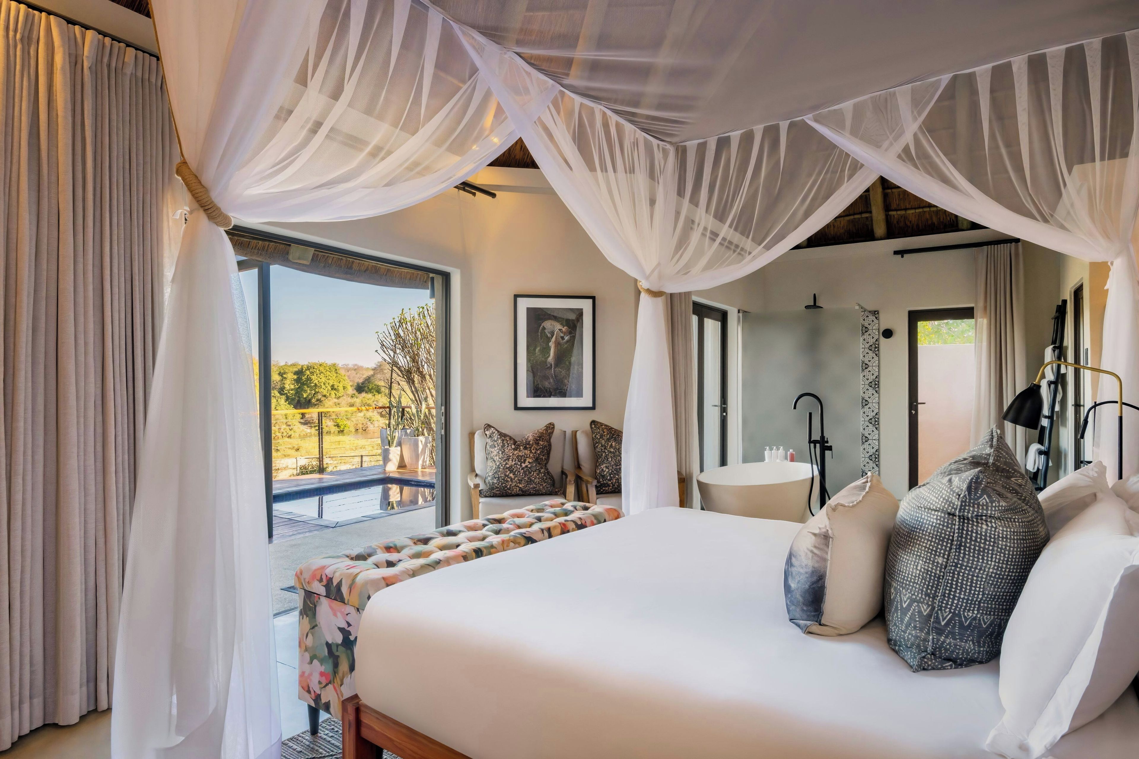 A bedroom with a large bed, a bathroom with a sink, and a view of the outdoors.
