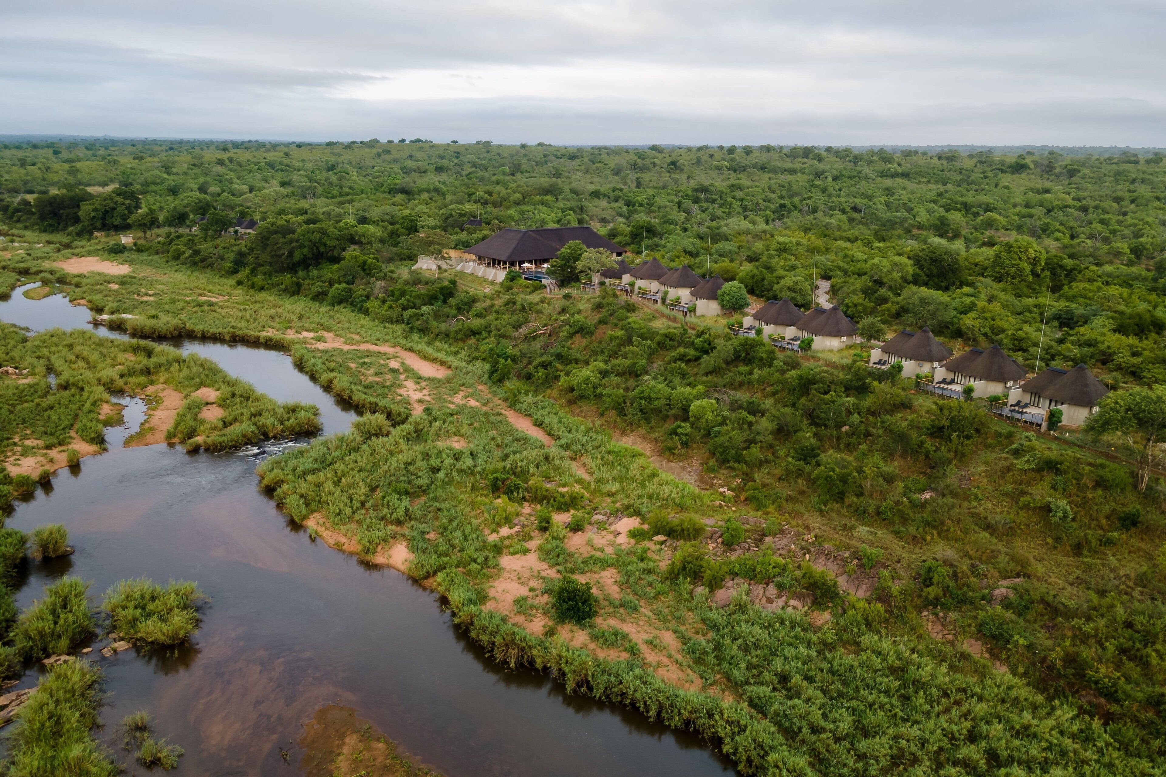 A rural area with a river, surrounded by dense greenery and several thatched-roof buildings.