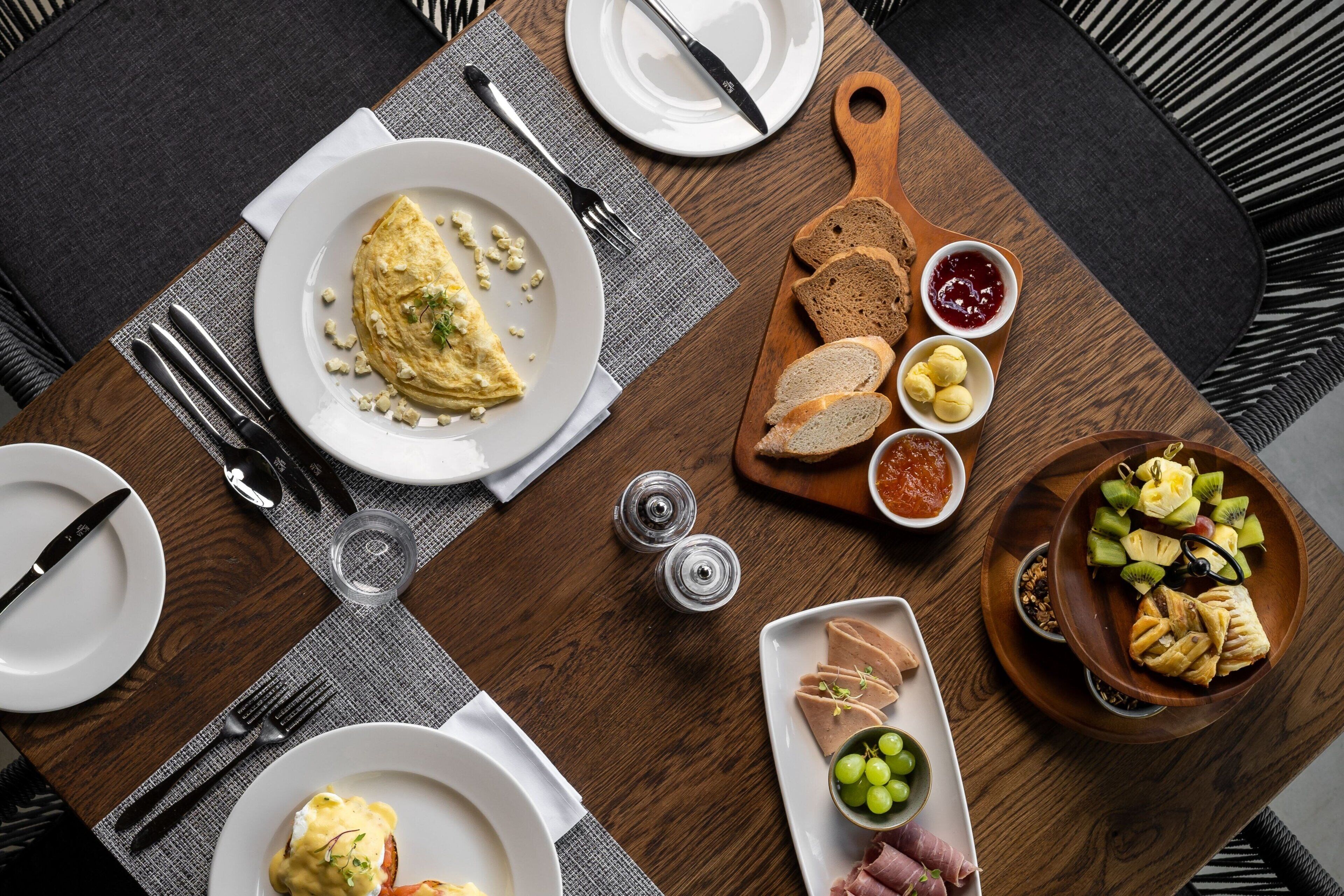 Una mesa de comedor con diferentes alimentos, platos, cubiertos y una servilleta.