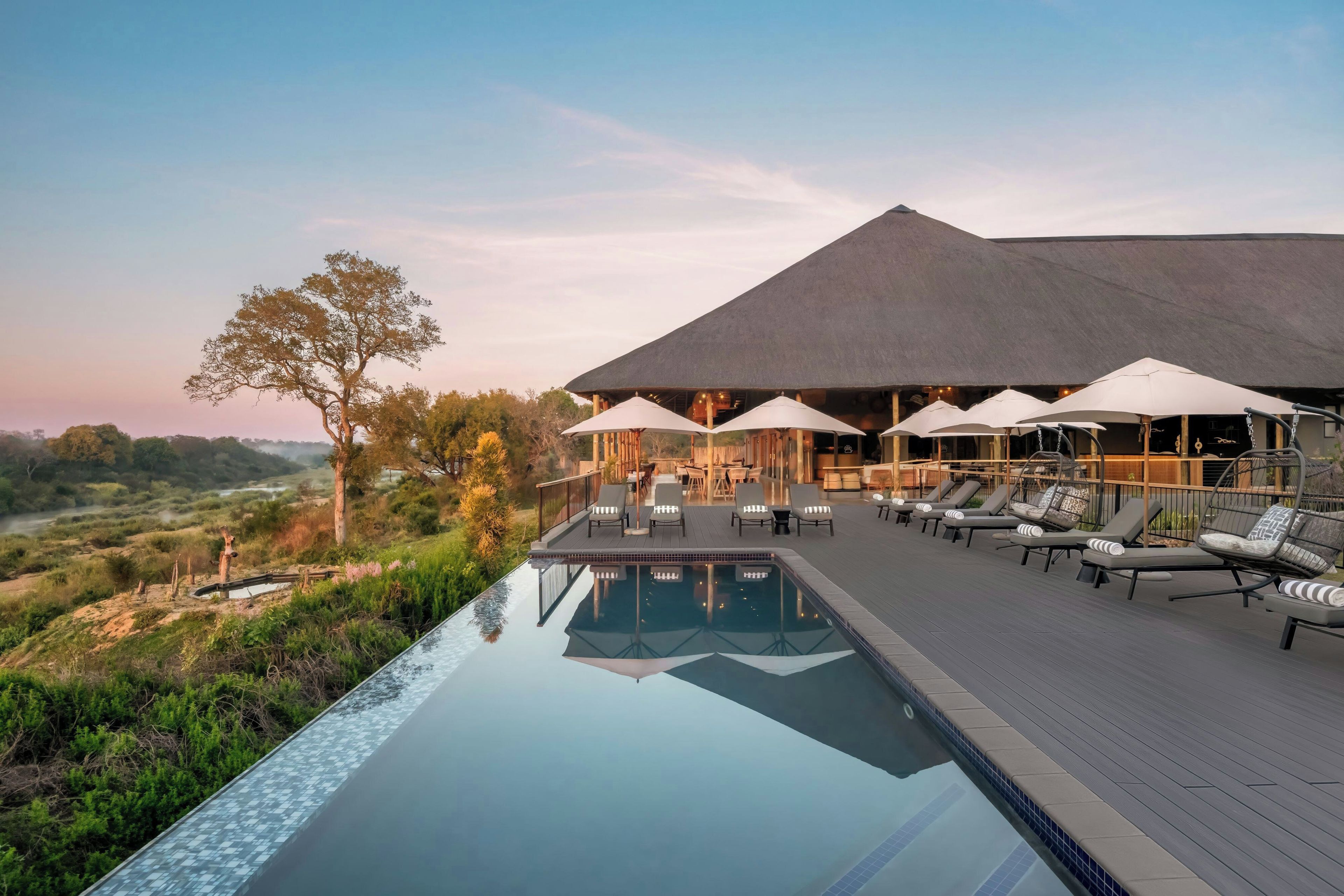 An infinity pool with lounge chairs and umbrellas, overlooking a natural landscape.