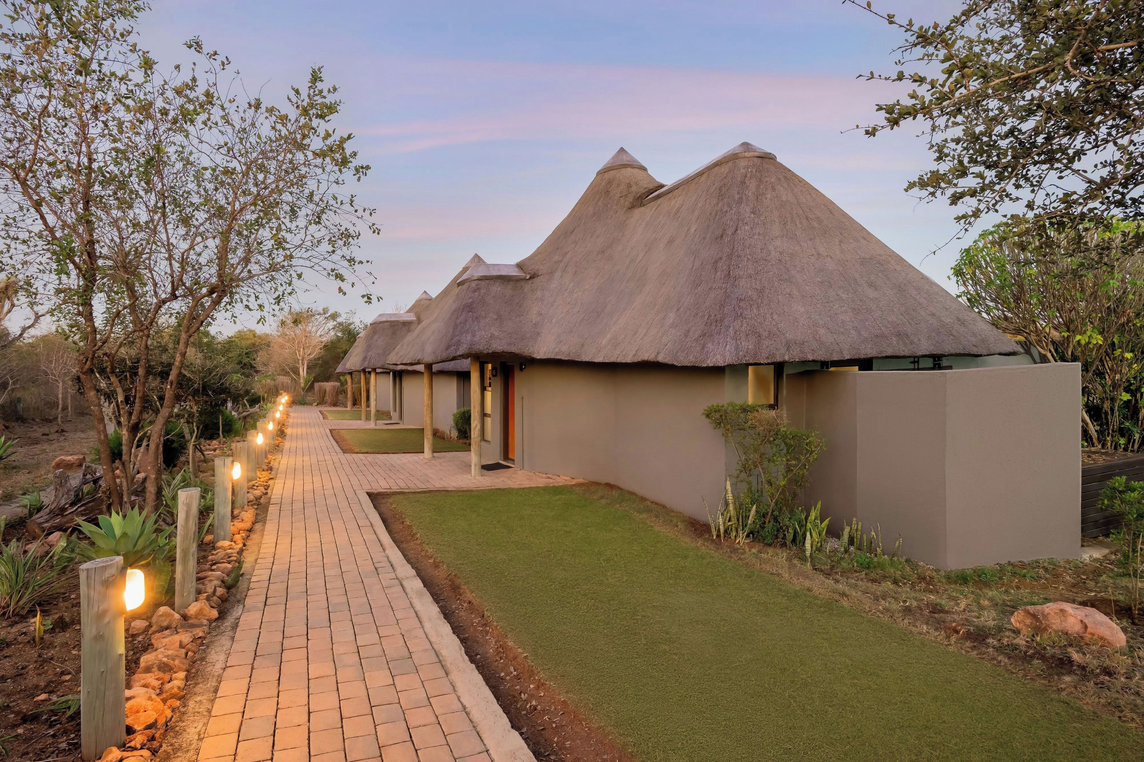A row of thatched-roof cottages with a paved walkway leading to the entrance.