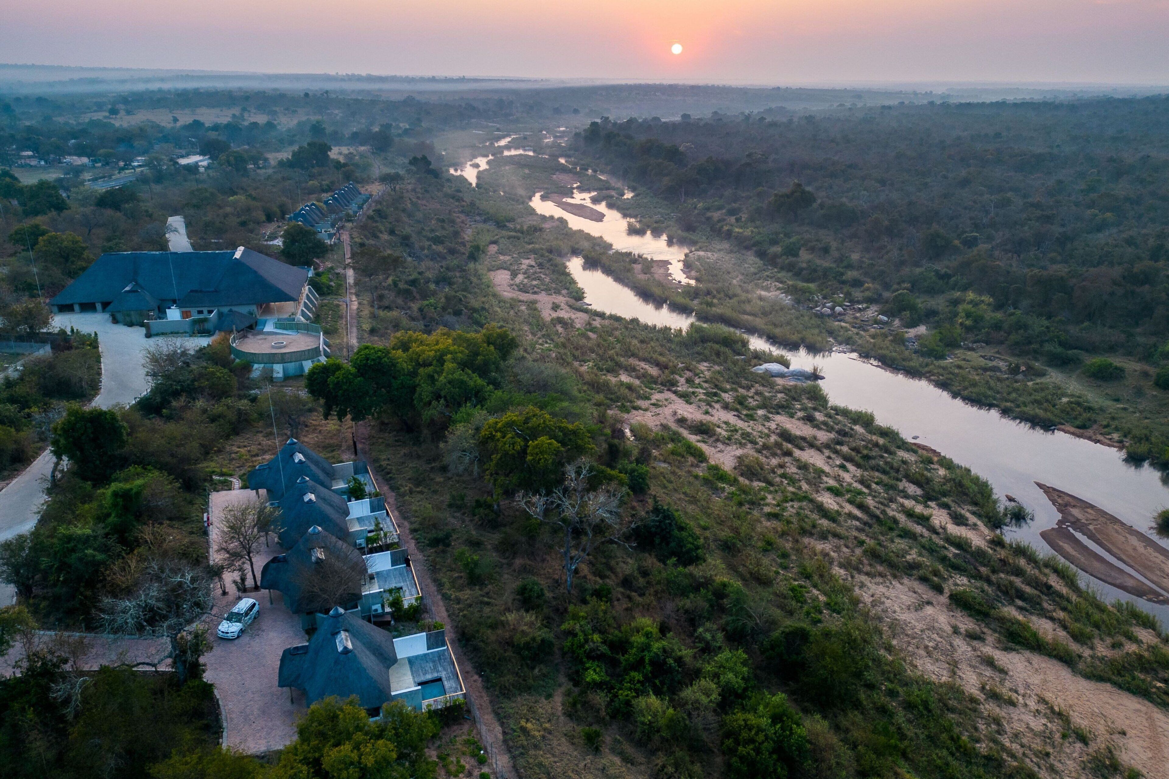 An aerial view of a resort with multiple buildings, a river, and surrounding vegetation.