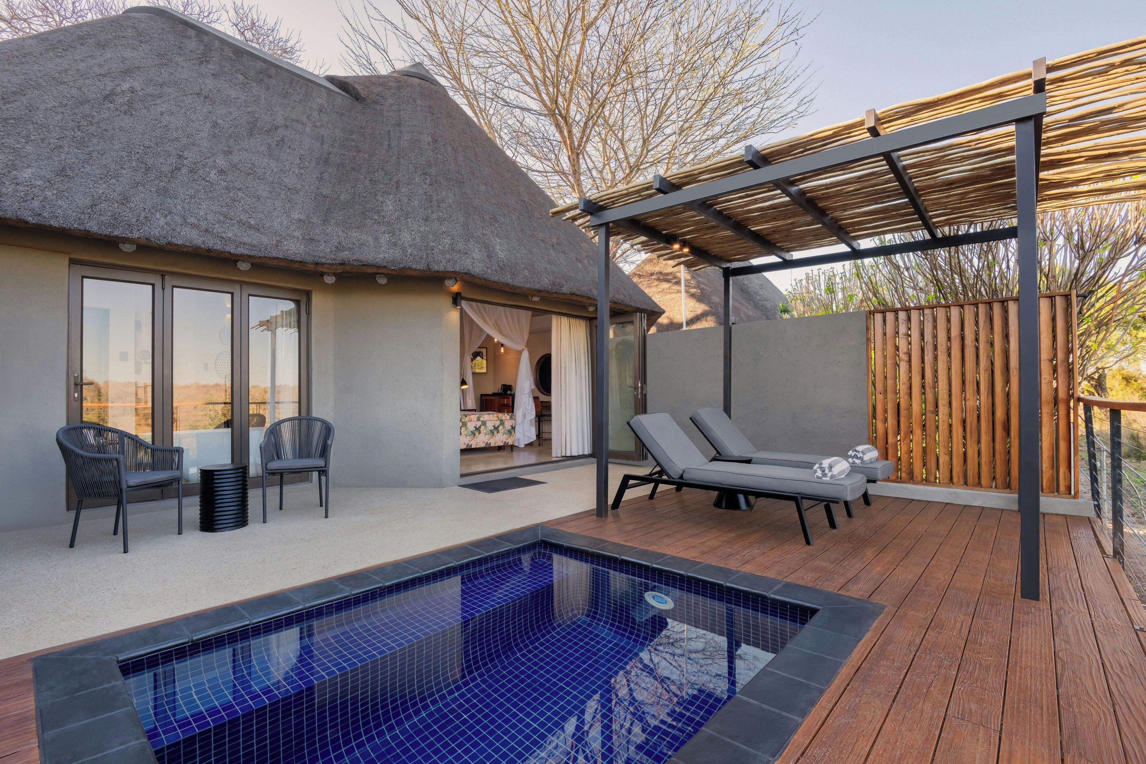 A pool area with a thatched-roof structure, lounge chairs, and a wooden deck.