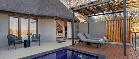 A pool area with a thatched-roof structure, lounge chairs, and a wooden deck.