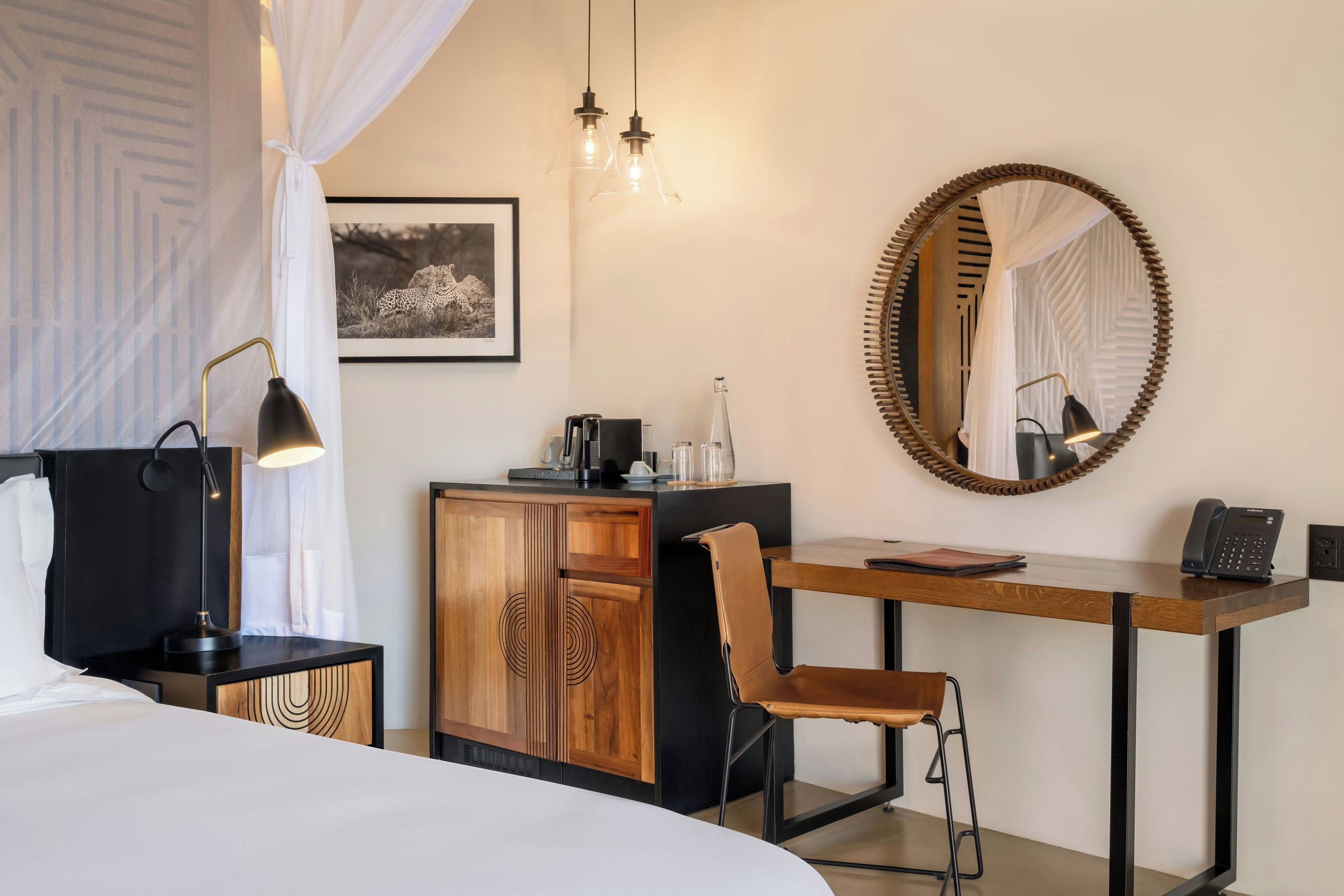 A hotel room with a bed, a desk with a chair, a mirror, and a picture on the wall.