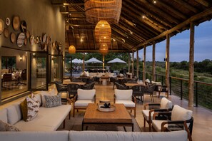 An outdoor seating area with wicker furniture, a wooden coffee table, and a view of the landscape. - Leopard Sands Kruger Park, Autograph Collection (Mbombela)