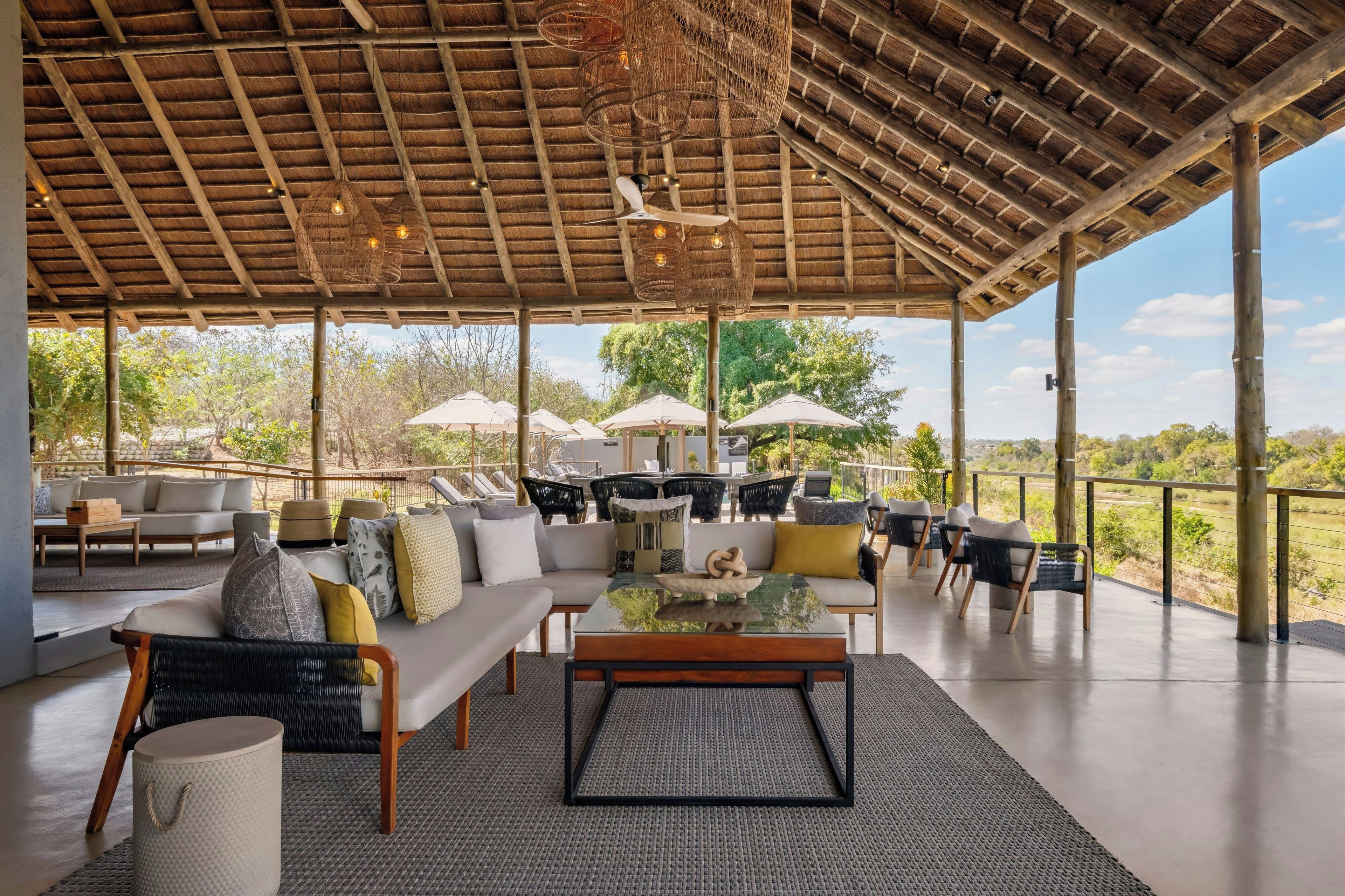 An open-air lounge with a thatched roof, outdoor seating, and a view of the landscape.