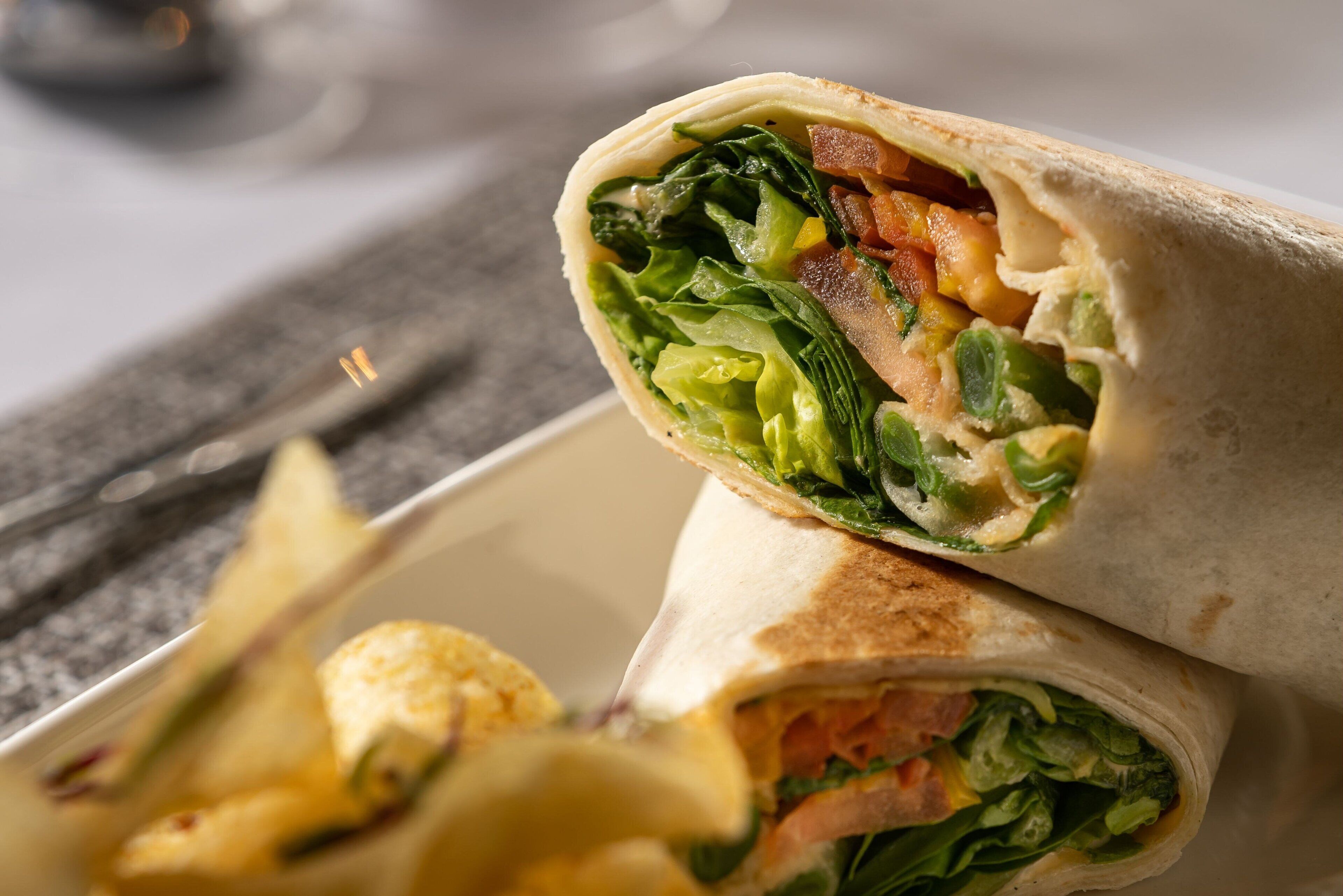 A burrito with visible fillings of lettuce, tomatoes, and possibly cheese, served in a white bowl.