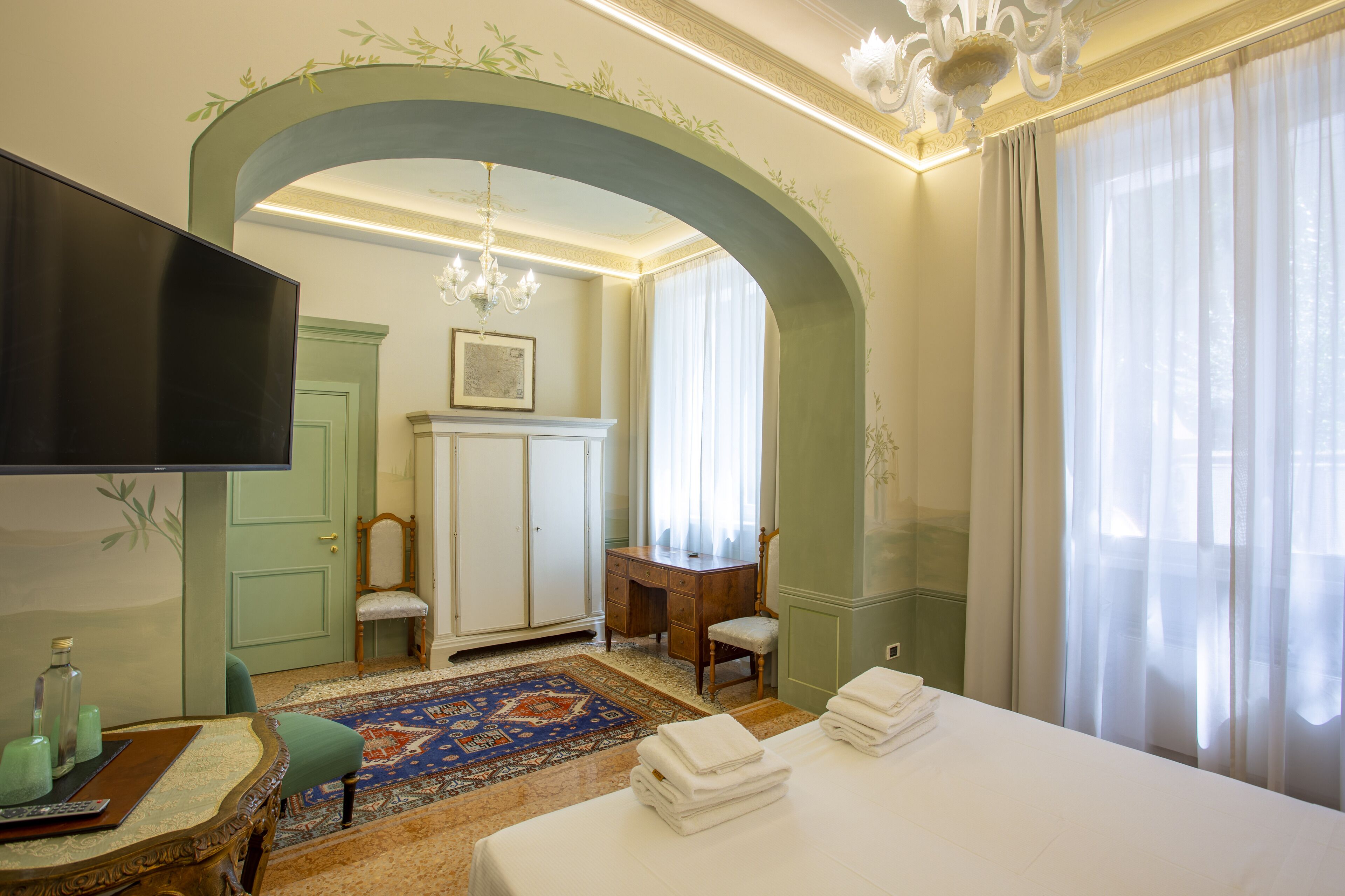 A hotel room with a bed, a desk, a chair, a television, and a large window with curtains.